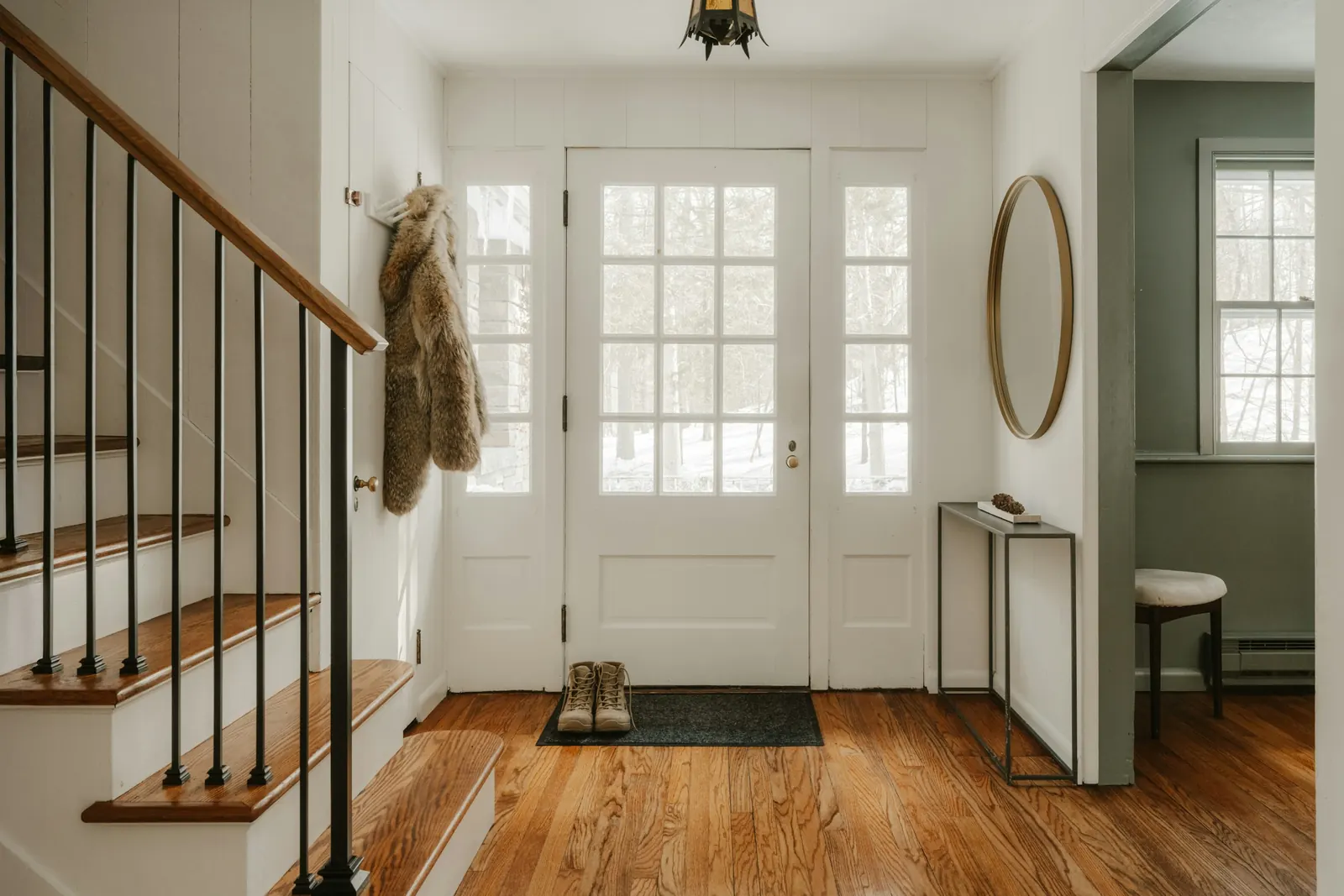 Tidy home entryway with a white front door, wooden stairs and a round mirror