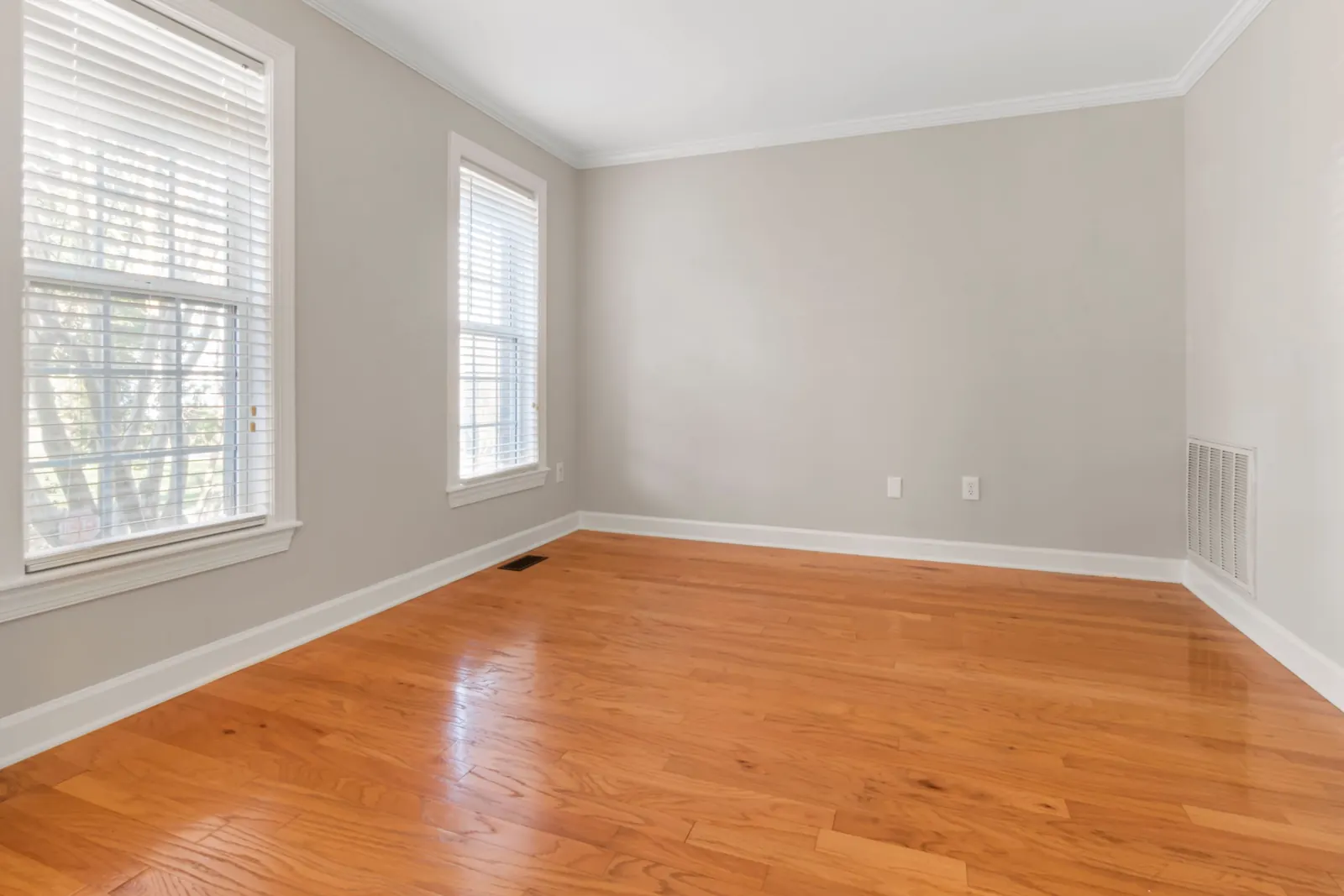 Empty room with beige walls, white window blinds and a shiny hardwood floor