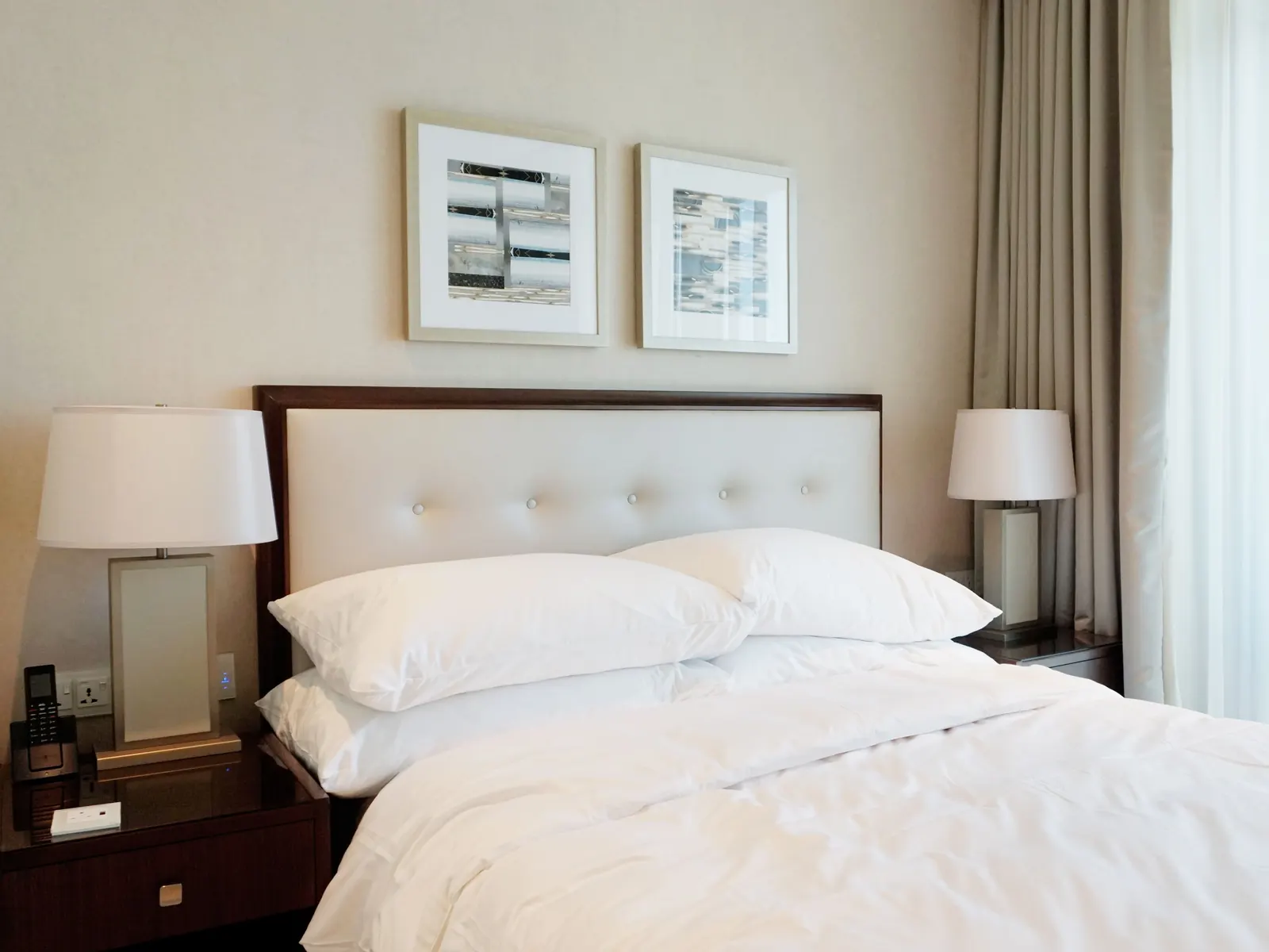 Neatly made bed with crisp white linens, bedside lamps and framed prints