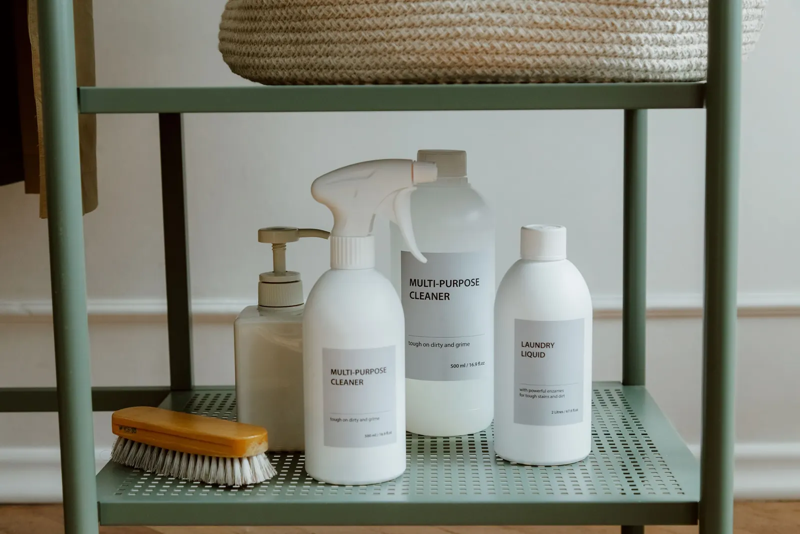 Unbranded white cleaning bottles and a wooden scrub brush on a green shelf
