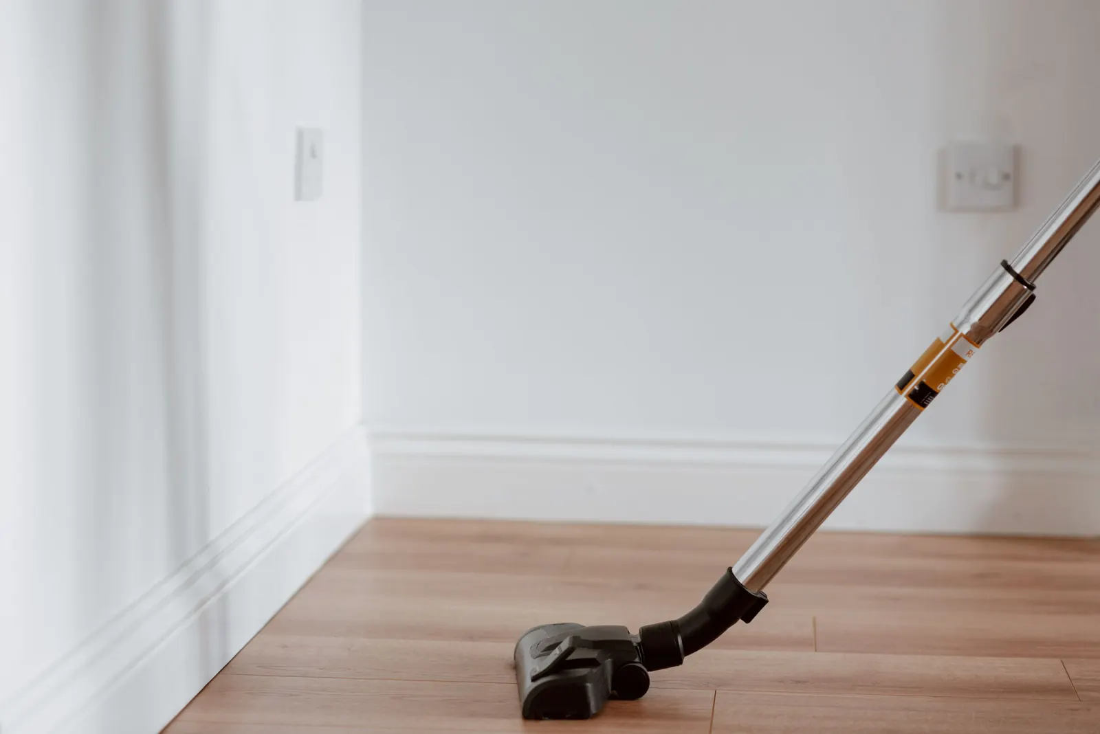 Vacuum cleaner head on a light wooden floor next to a white wall