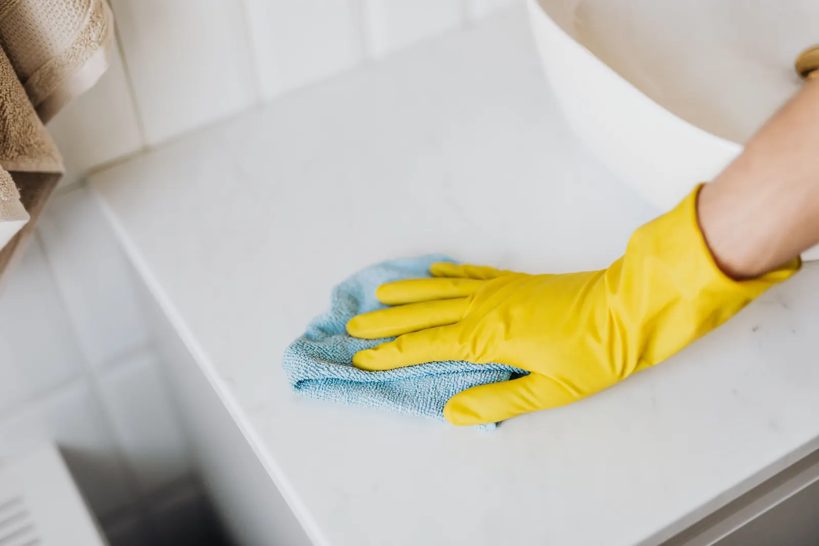 Gloved hand wiping a white counter with a blue microfibre cloth